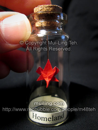 Miniture red origami maple leaf in a small bottle, with the word 'Homeland'; written below on a yellow label. Origami design by Mui-Ling Teh